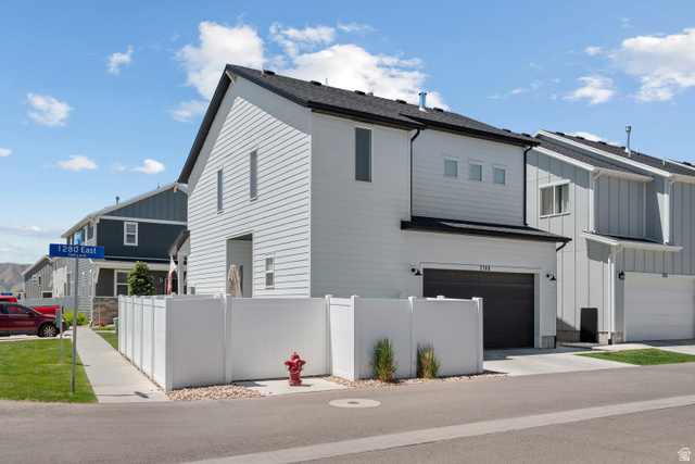 1708 North 1280th Street East Payson, UT 84651 - Photo 15 of 15 Modern townhome exterior featuring white horizontal siding, a dark asphalt shingle roof, a black garage door, and a white privacy fence