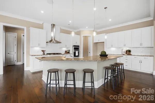 a kitchen with stainless steel appliances granite countertop a stove top oven a sink a refrigerator and white cabinets with wooden floor