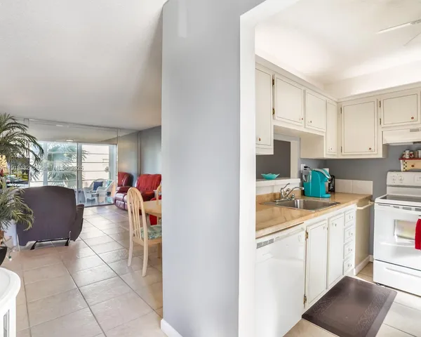 a living room with stainless steel appliances furniture a rug and a kitchen