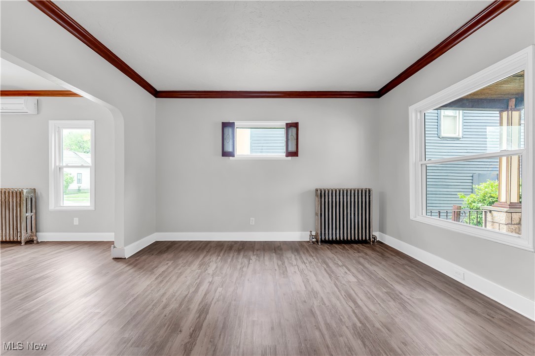 3374 Fulton Road Cleveland, OH 44109 - Photo 5 of 27 Spare room featuring radiator heating unit, wood finished floors, ornamental molding, and a wall unit AC