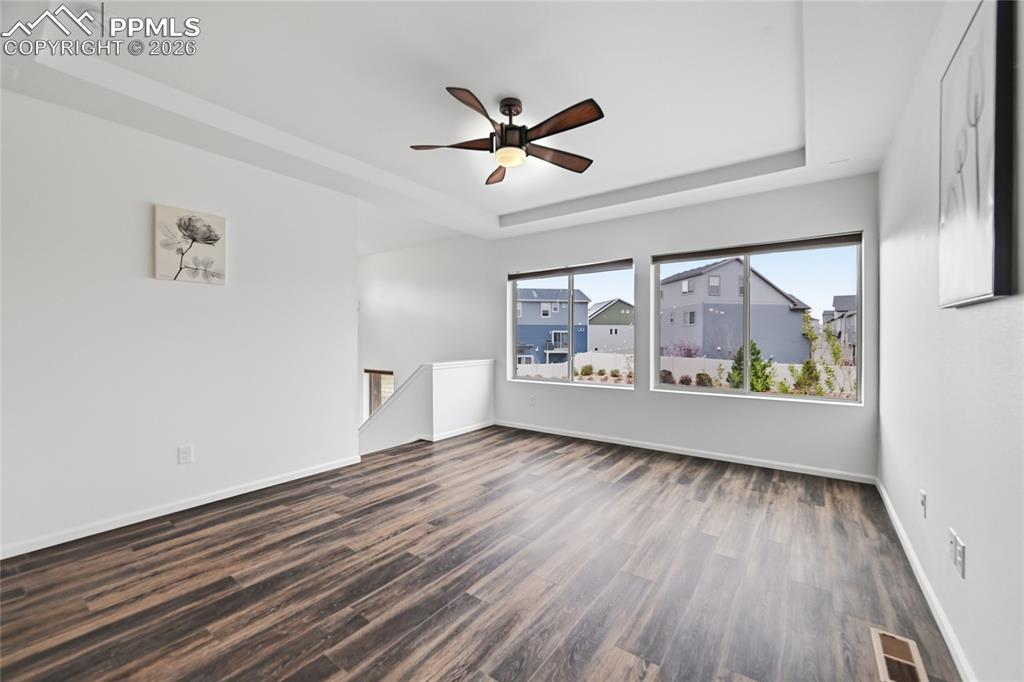 9414 Timberlake Loop Colorado Springs, CO 80927 - Photo 8 of 40 Unfurnished living room featuring two big windows, a raised ceiling, a ceiling fan, and dark luxury vinyl wood finished floors