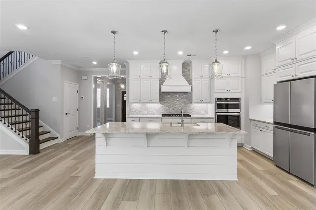 a large white kitchen with a refrigerator a kitchen island a stove and white cabinets with wooden floor