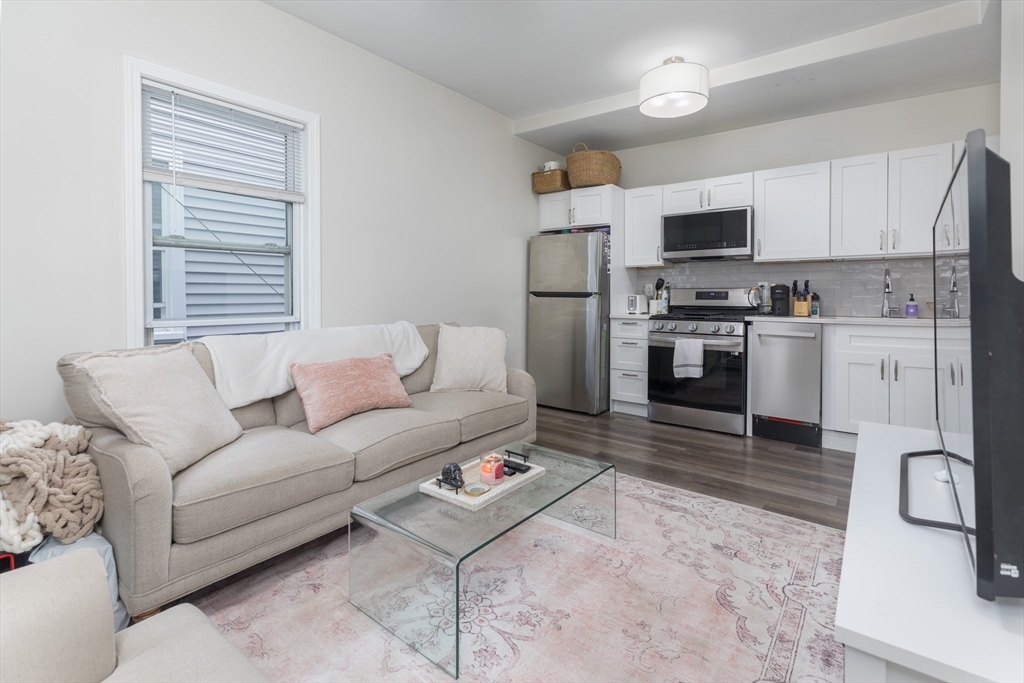 a living room with stainless steel appliances furniture and a kitchen view