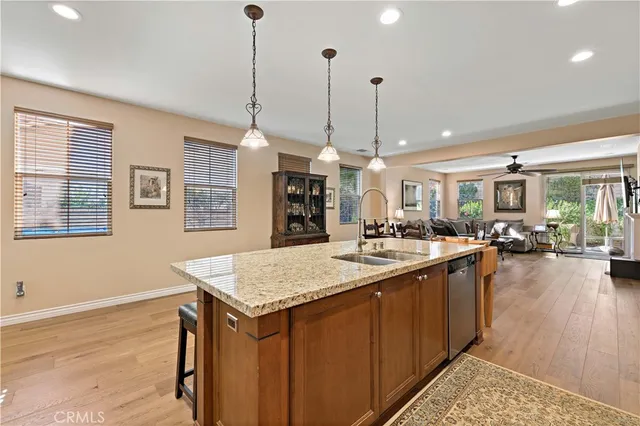 a kitchen with stainless steel appliances kitchen island granite countertop a refrigerator a stove a sink a dining table and chairs with wooden floor