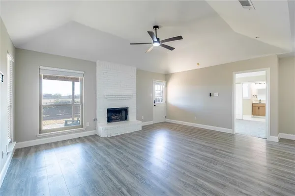 an empty room with wooden floor a ceiling fan and windows