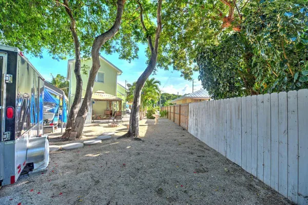 a view of a street with large trees and a wooden fence