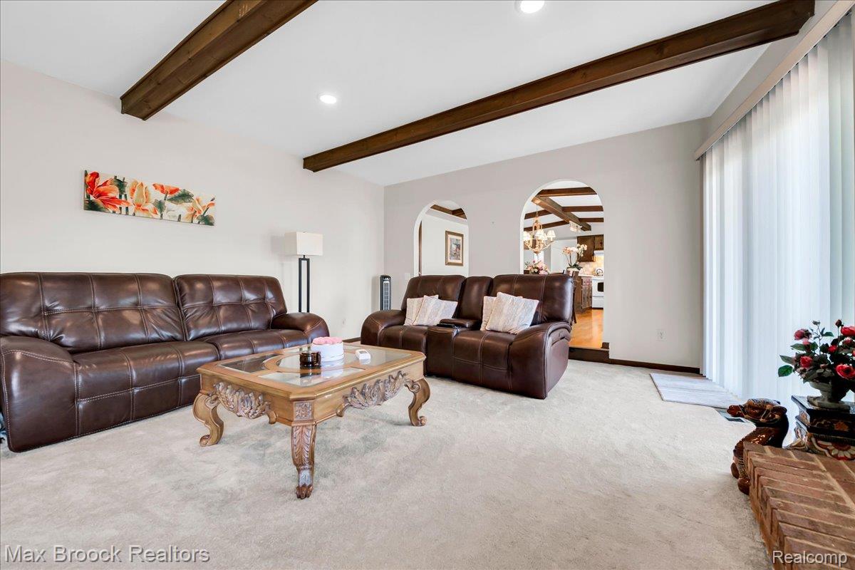 217 Stonetree Circle Rochester, MI 48309 - Photo 23 of 44 Living room featuring exposed wood ceiling beams, neutral wall tones, arched doorways, light-toned carpeting, and a full-height window with vertical blinds