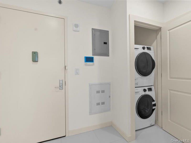 124-28 Queens Boulevard, Unit 12A Queens, NY 11415 - Photo 13 of 16 Laundry area featuring electric panel, stacked washer / dryer, and light tile patterned flooring