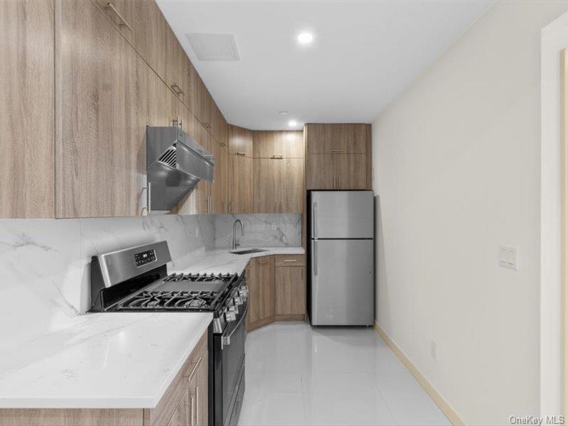 124-28 Queens Boulevard, Unit 12A Queens, NY 11415 - Photo 7 of 16 Kitchen featuring stainless steel appliances, modern cabinets, decorative backsplash, under cabinet range hood, and light stone countertops