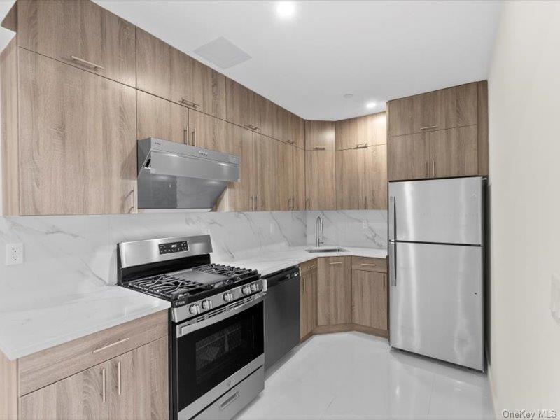 124-28 Queens Boulevard, Unit 12A Queens, NY 11415 - Photo 8 of 16 Kitchen featuring stainless steel appliances, under cabinet range hood, light stone counters, light tile patterned flooring, and tasteful backsplash