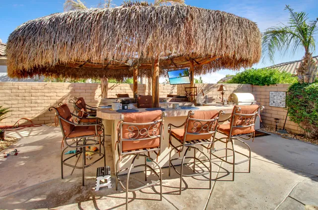 a view of a patio with table and chairs under an umbrella with a barbeque