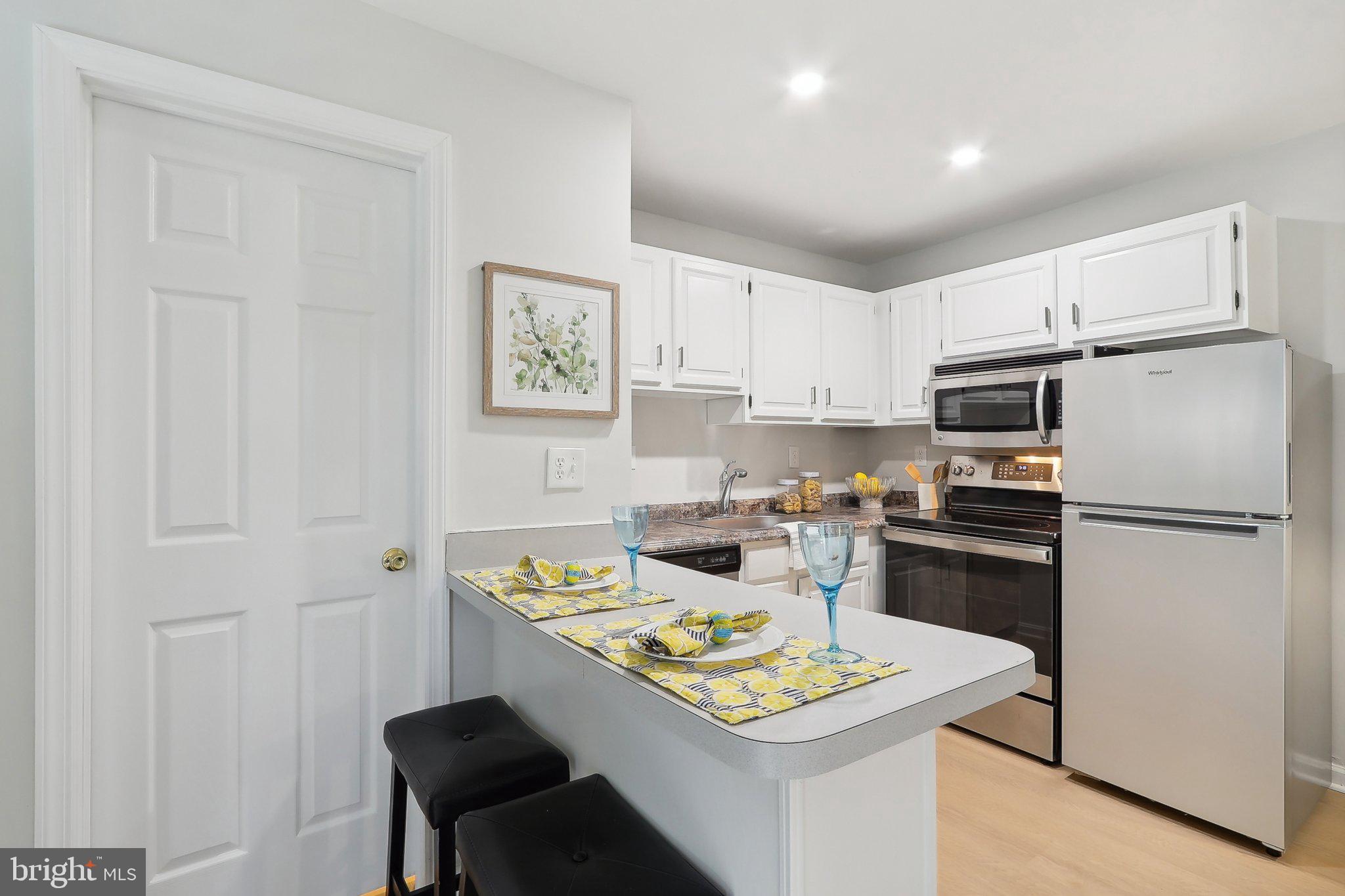 6638 A Hillandale Road, Unit 53A Chevy Chase, MD 20815 - Photo 6 of 26 a kitchen with a refrigerator a stove a sink dishwasher and white cabinets with wooden floor
