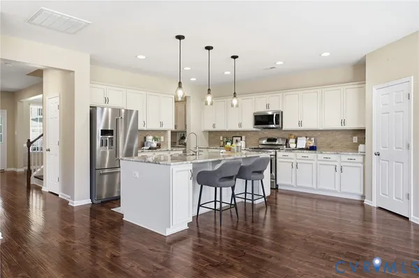 a kitchen with stainless steel appliances kitchen island granite countertop a refrigerator a stove a oven and white cabinets with wooden floor