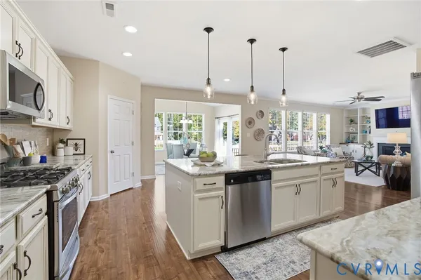 a kitchen with stainless steel appliances granite countertop a stove top oven a sink a dining table and chairs with wooden floor