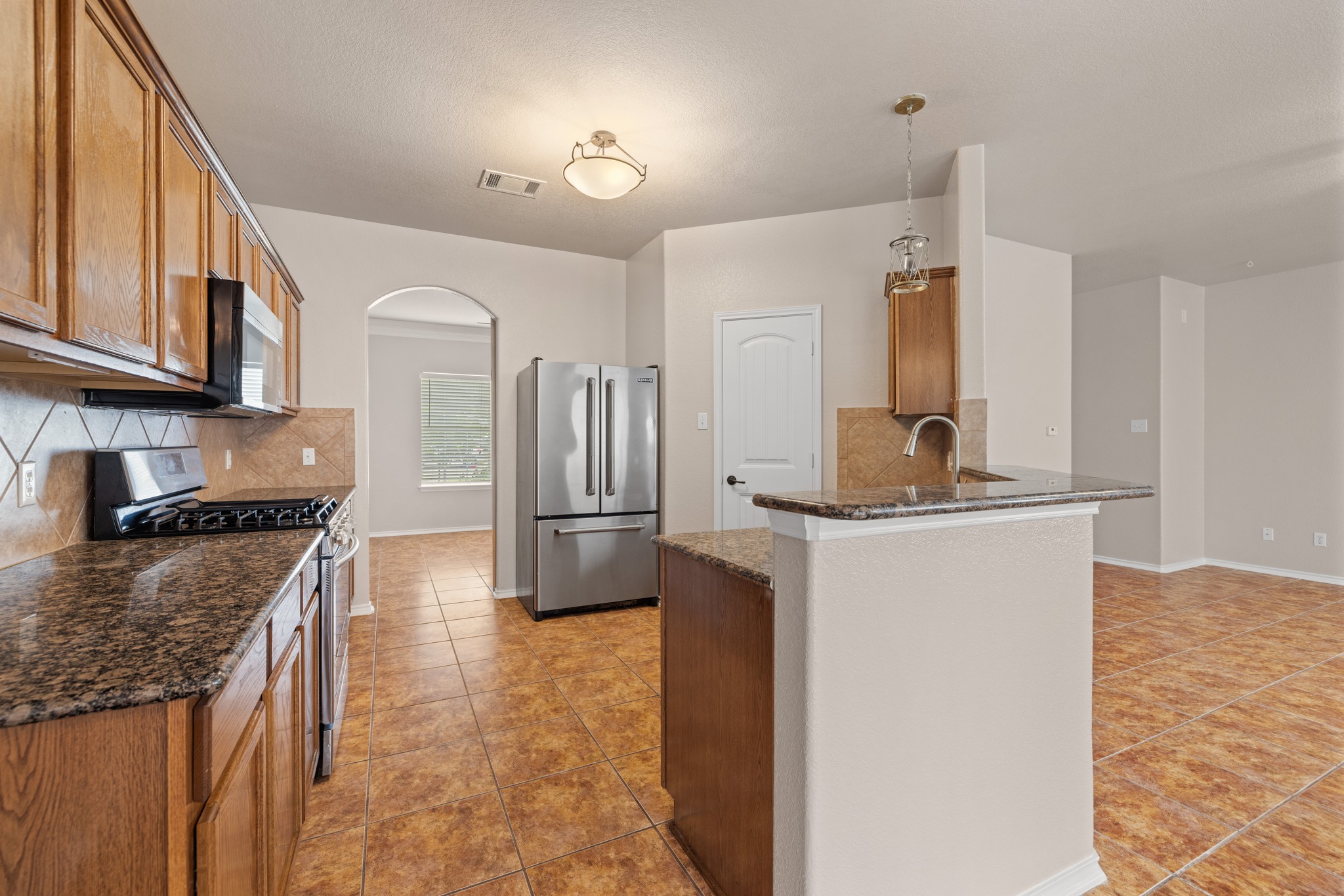 403 Red Hawk Drive Leander, TX 78641 - Photo 11 of 37 Kitchen featuring wood cabinetry, stainless steel appliances, granite countertops, and ceramic tile flooring
