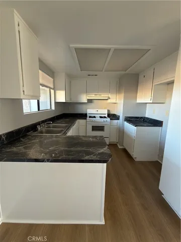 a large kitchen with granite countertop a stove a sink a refrigerator and white cabinets