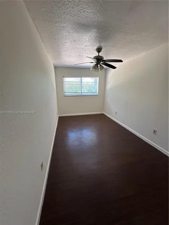 a view of an empty room with wooden floor and a ceiling fan