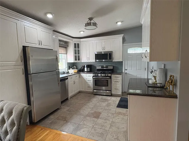 a kitchen with granite countertop a refrigerator a sink a stove top oven and cabinets