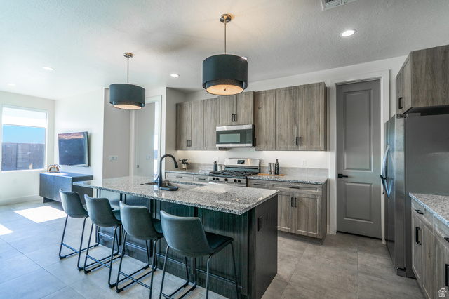 2972 West 570 North Hurricane, UT 84737 - Photo 22 of 104 Kitchen featuring light stone countertops, stainless steel appliances, a kitchen bar, a kitchen island with sink, and a textured ceiling