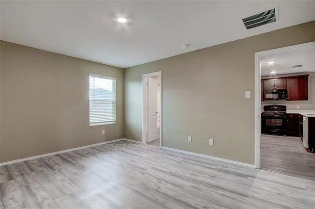 a view of empty room with wooden floor and kitchen