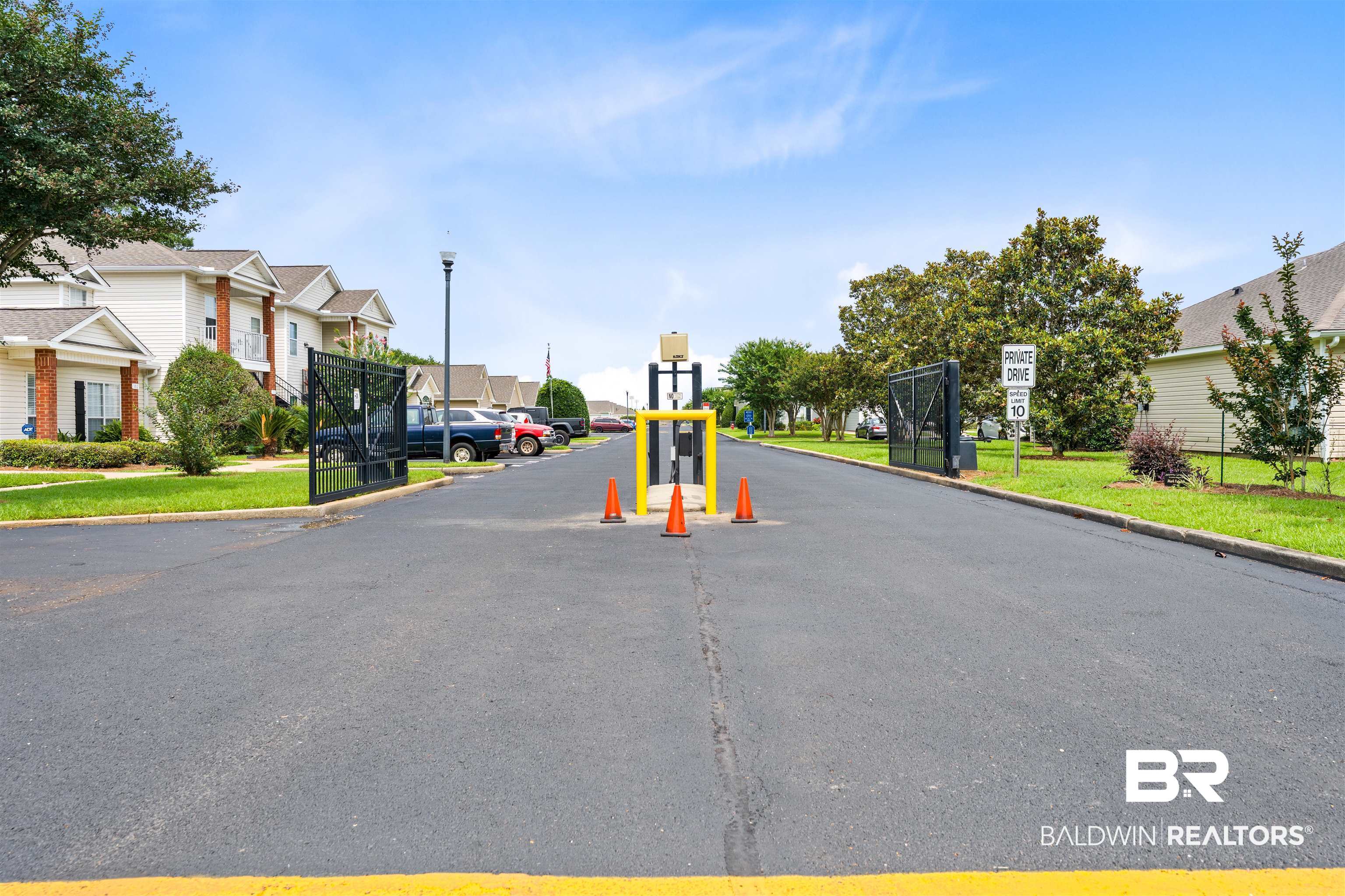 2651 South Juniper Street, Unit 1801 Foley, AL 36535 - Photo 4 of 16 Gated community entrance with asphalt drive, featuring black wrought iron gates, a yellow gate arm, and street lighting