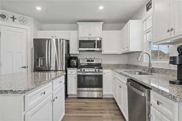 a kitchen with granite countertop a sink stainless steel appliances and white cabinets