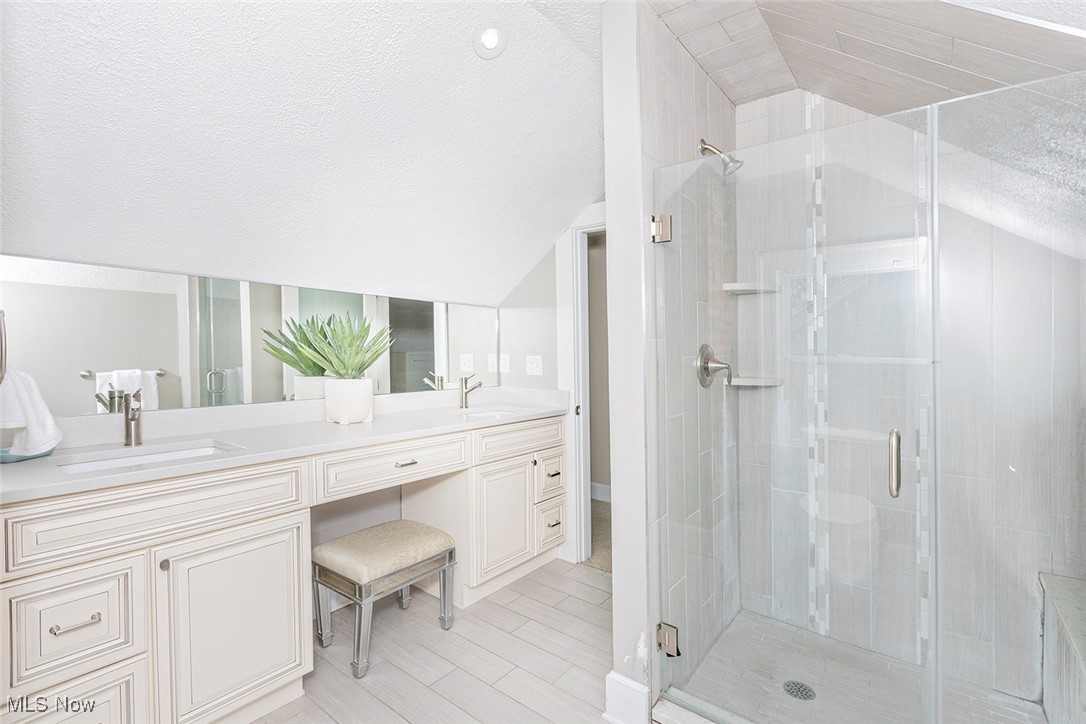2875 Coleridge Road Cleveland, OH 44118 - Photo 25 of 37 Bathroom with lofted ceiling, a textured ceiling, a shower stall, double vanity, and light wood finished floors