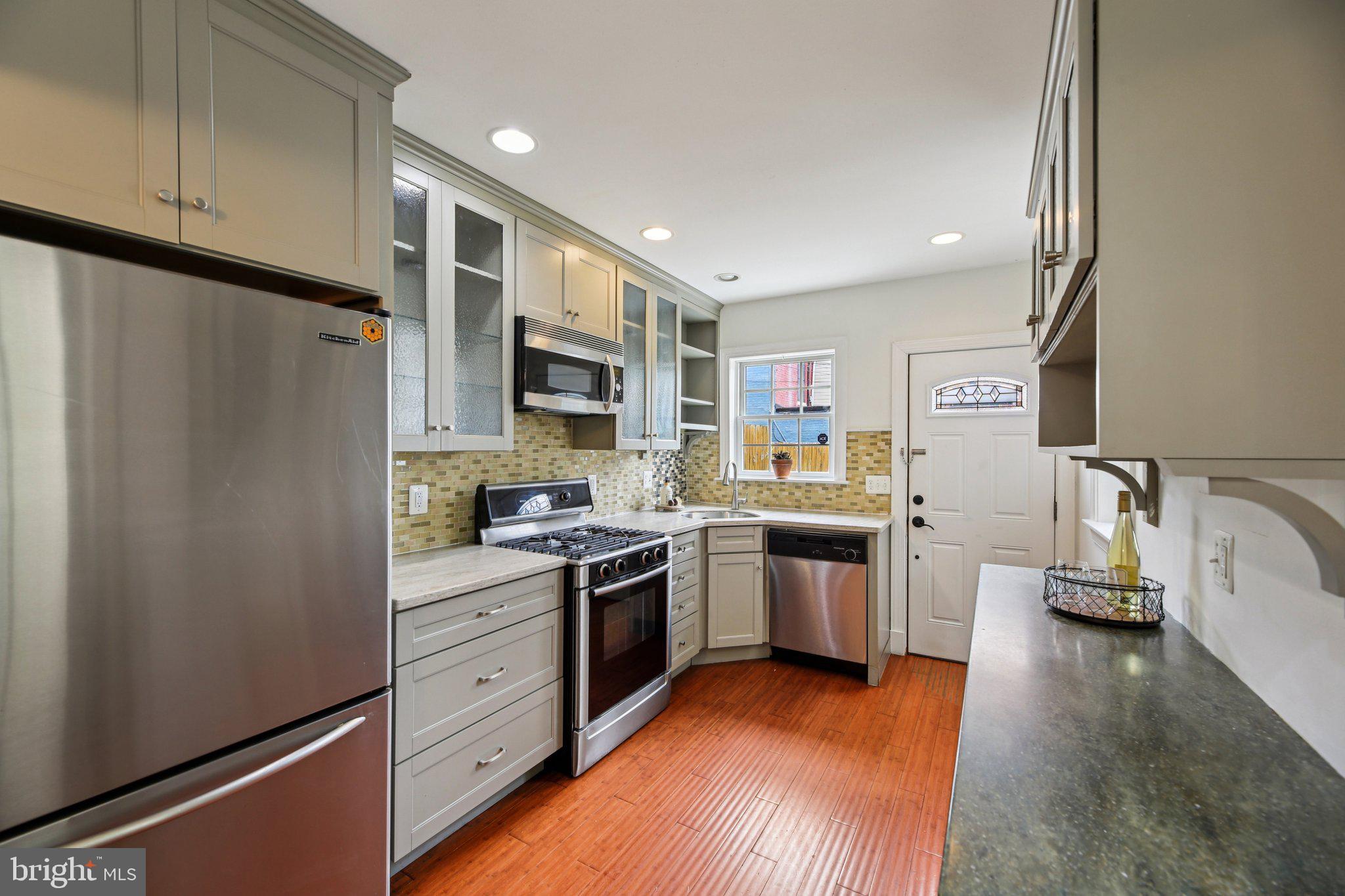 a kitchen with stainless steel appliances granite countertop a refrigerator a sink dishwasher a stove and white countertops with wooden floor