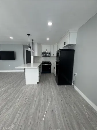 a living room with stainless steel appliances kitchen island granite countertop a refrigerator a stove a microwave and white cabinets