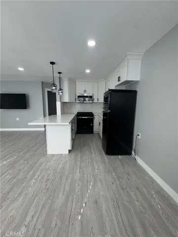 a living room with stainless steel appliances kitchen island granite countertop a refrigerator a stove a microwave and white cabinets