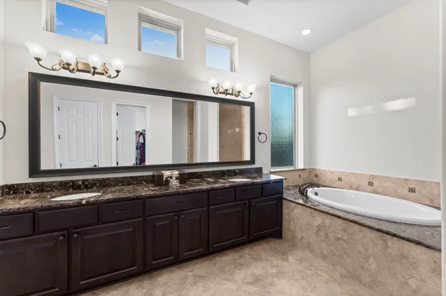 a bathroom with a granite countertop double vanity sink a mirror and bathtub