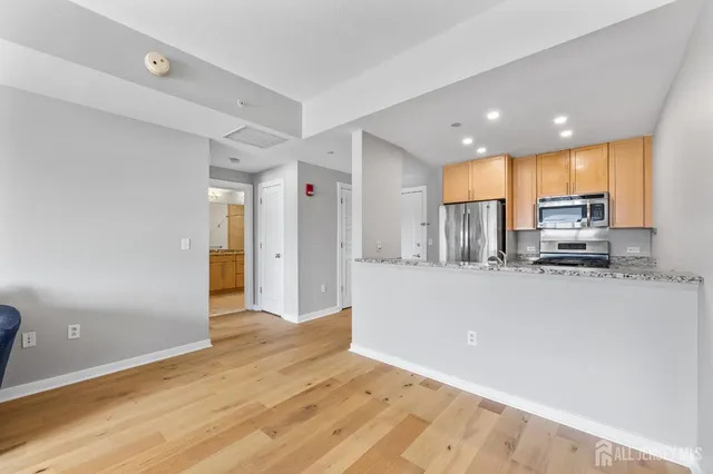 a living room with stainless steel appliances a refrigerator cabinets and wooden floor