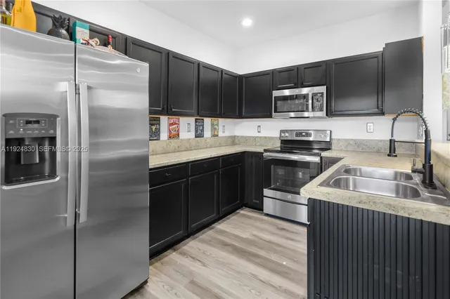 a kitchen with stainless steel appliances granite countertop a refrigerator a sink a stove top oven and wooden floors