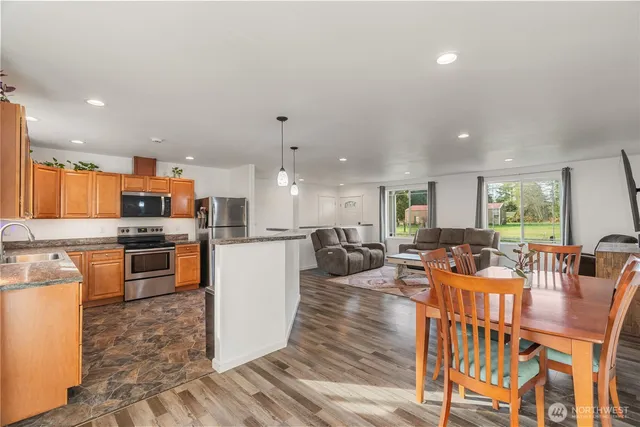 a open kitchen with stainless steel appliances kitchen island granite countertop a refrigerator a stove a sink dishwasher with a dining table and chairs with wooden floor