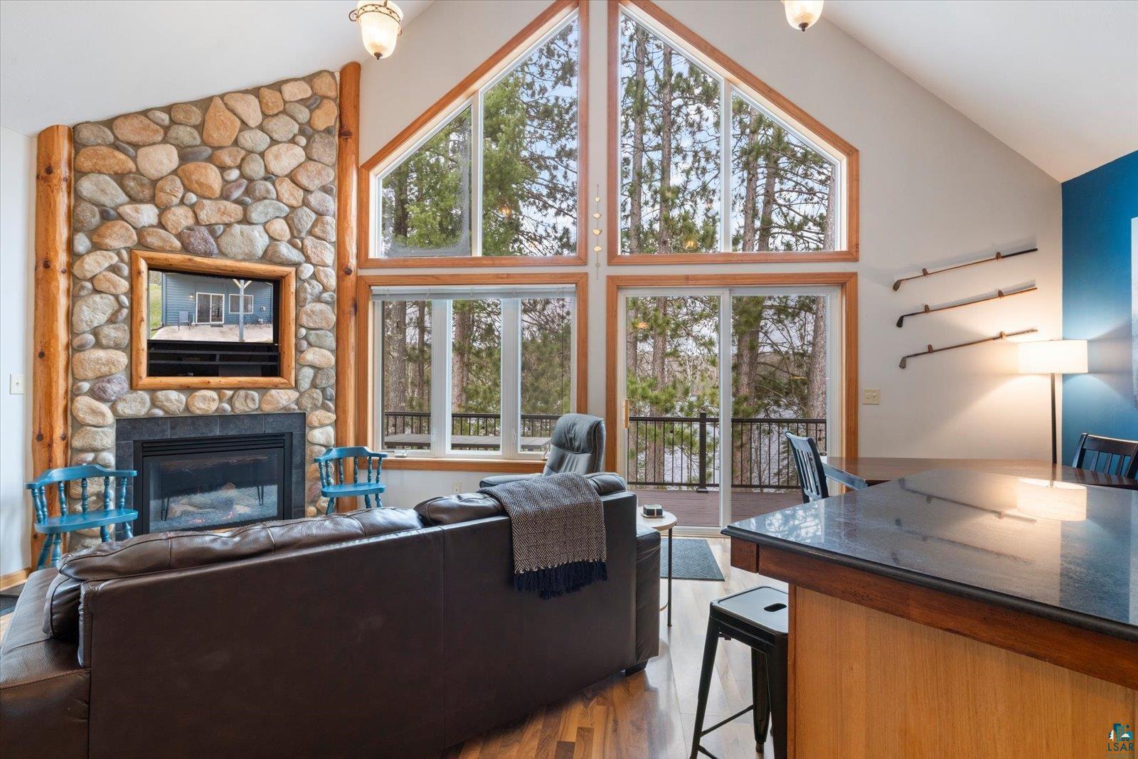 6266 Giants Ridge Road Biwabik, MN 55705 - Photo 10 of 37 Vaulted living space featuring a floor-to-ceiling stone fireplace with a wood mantel, expansive windows, wood-finish flooring, and a kitchen island with a dark countertop