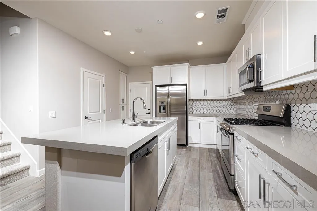 1174 Delpy View Point, Unit 102 Vista, CA 92084 - Photo 8 of 17 a kitchen with a sink a stove top oven a refrigerator and white cabinets