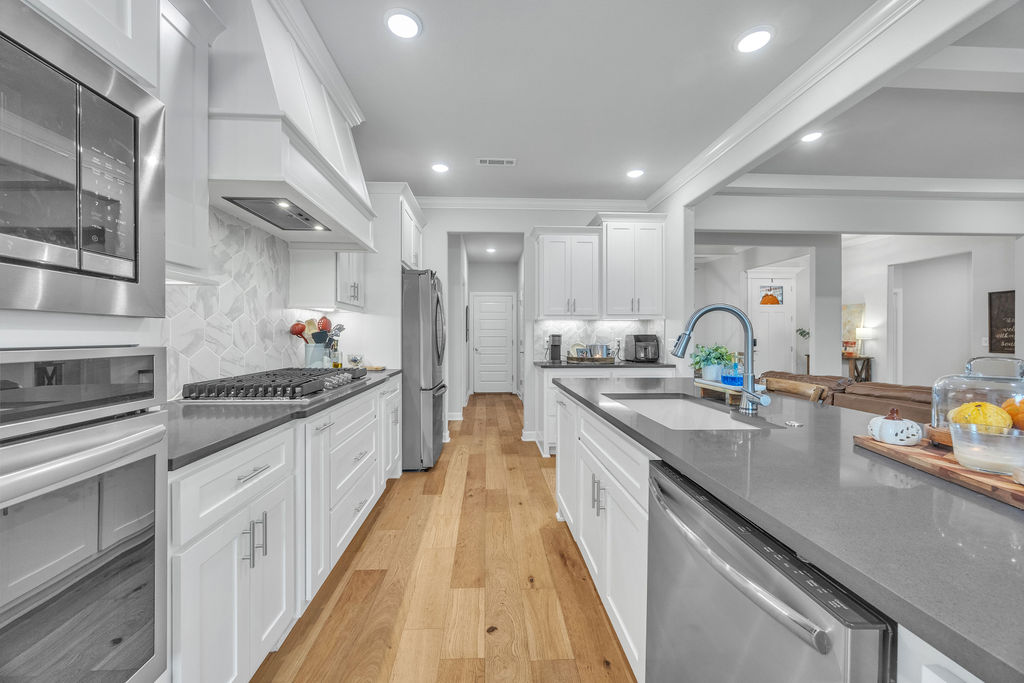 418 Casella Street Springdale, AR 72762 - Photo 11 of 34 Gourmet kitchen featuring a center island with sink, white cabinetry, integrated stainless steel appliances, a range hood, and wood-finish flooring