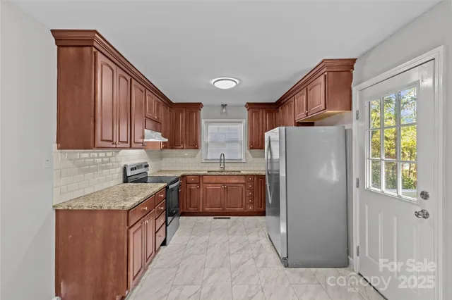 a kitchen with stainless steel appliances granite countertop a refrigerator a sink dishwasher and wooden cabinets with wooden floor