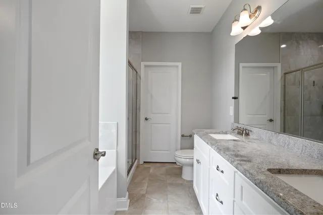 a bathroom with a granite countertop double vanity sink a mirror and a shower