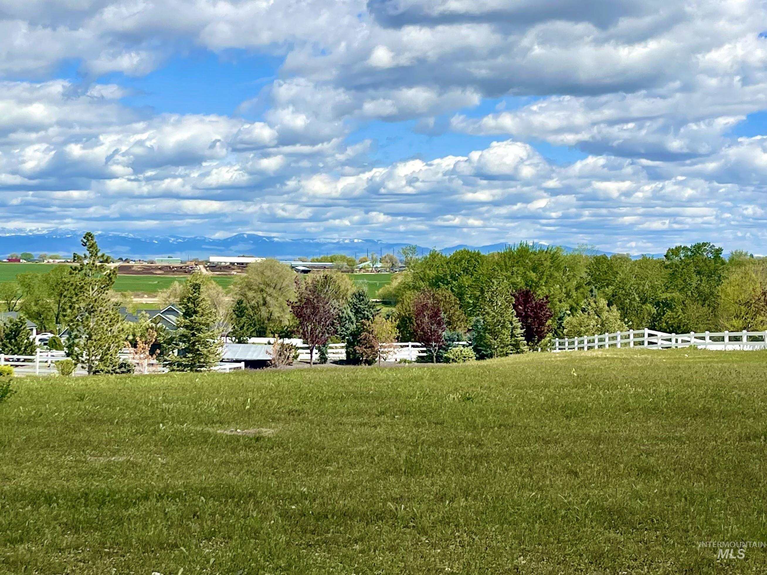 15015 Leon Lane Caldwell, ID 83607 - Photo 39 of 44 Expansive green field with a white picket fence, mature trees, and distant snow-capped mountains