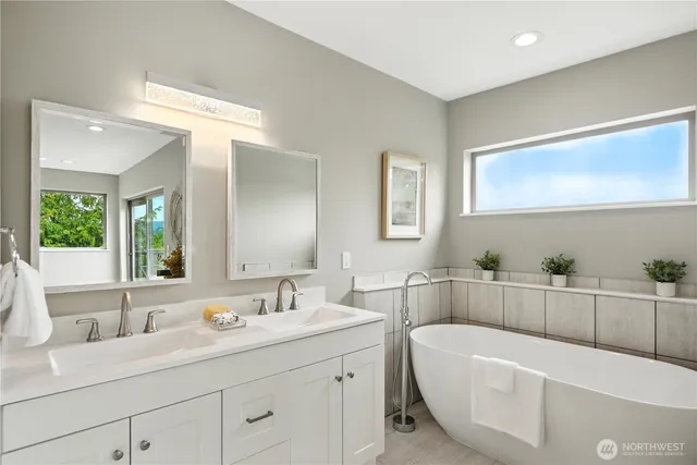 a bathroom with a bathtub a double vanity sink a window and mirror