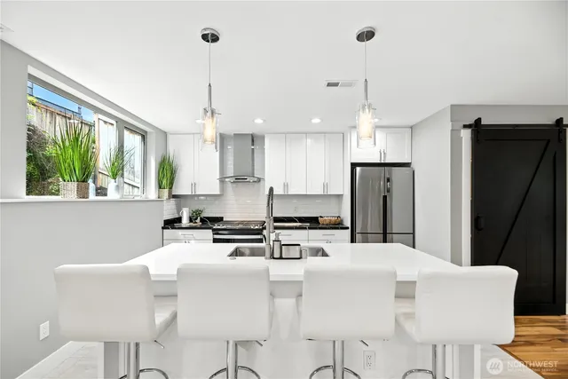 a kitchen with stainless steel appliances kitchen island granite countertop a dining table chairs and a refrigerator