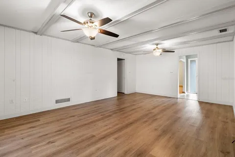 a view of an empty room with wooden floor and a kitchen