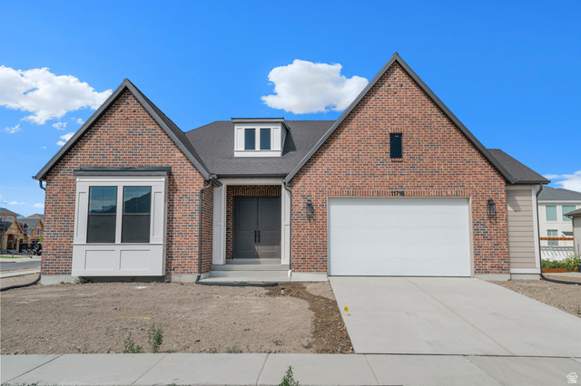Traditional home with driveway, a garage, brick siding, and roof with shingles