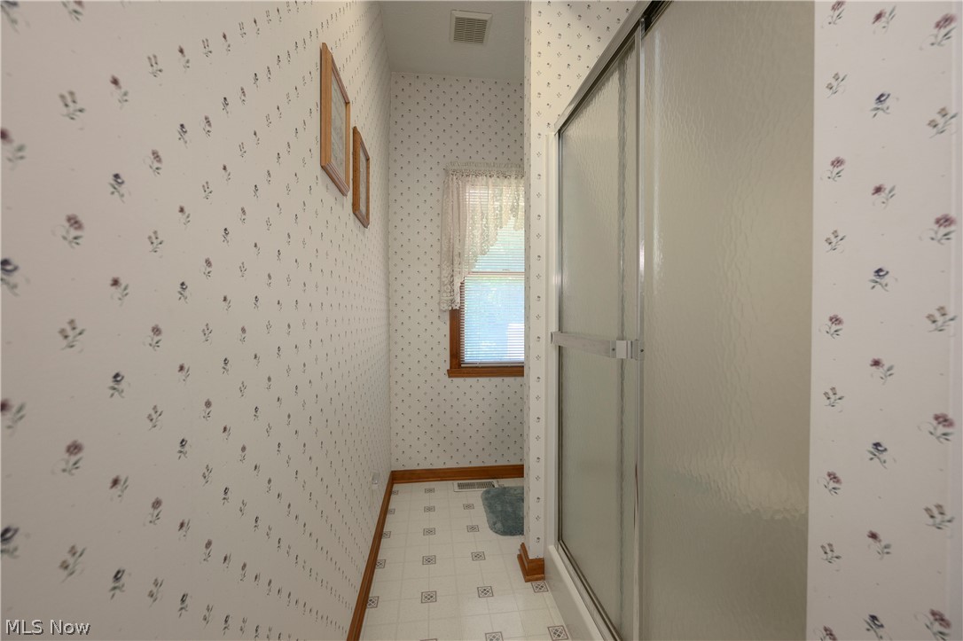 8745 Broadview Road Broadview Heights, OH 44147 - Photo 18 of 49 Shower enclosure with frosted glass panels, patterned wallpaper, wood-framed window, white tile flooring, and wood baseboards