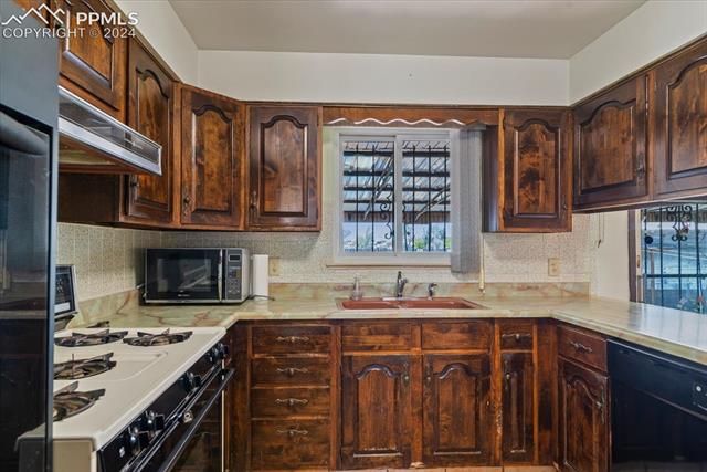 28018 County Farm Road Pueblo, CO 81006 - Photo 17 of 50 Kitchen with custom range hood, dark brown cabinets, sink, and black appliances