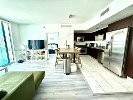 a dining hall with stainless steel appliances kitchen island granite countertop a table chairs and a sink