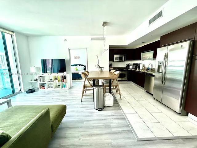 a dining hall with stainless steel appliances kitchen island granite countertop a table chairs and a sink