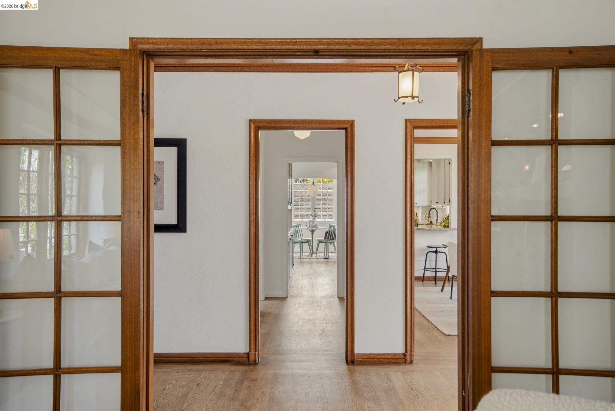 1087 Hubert Road Oakland, CA 94610 - Photo 8 of 67 Hallway with wood-finish flooring, featuring multiple doorways with wood trim and a glass-paneled double door entrance