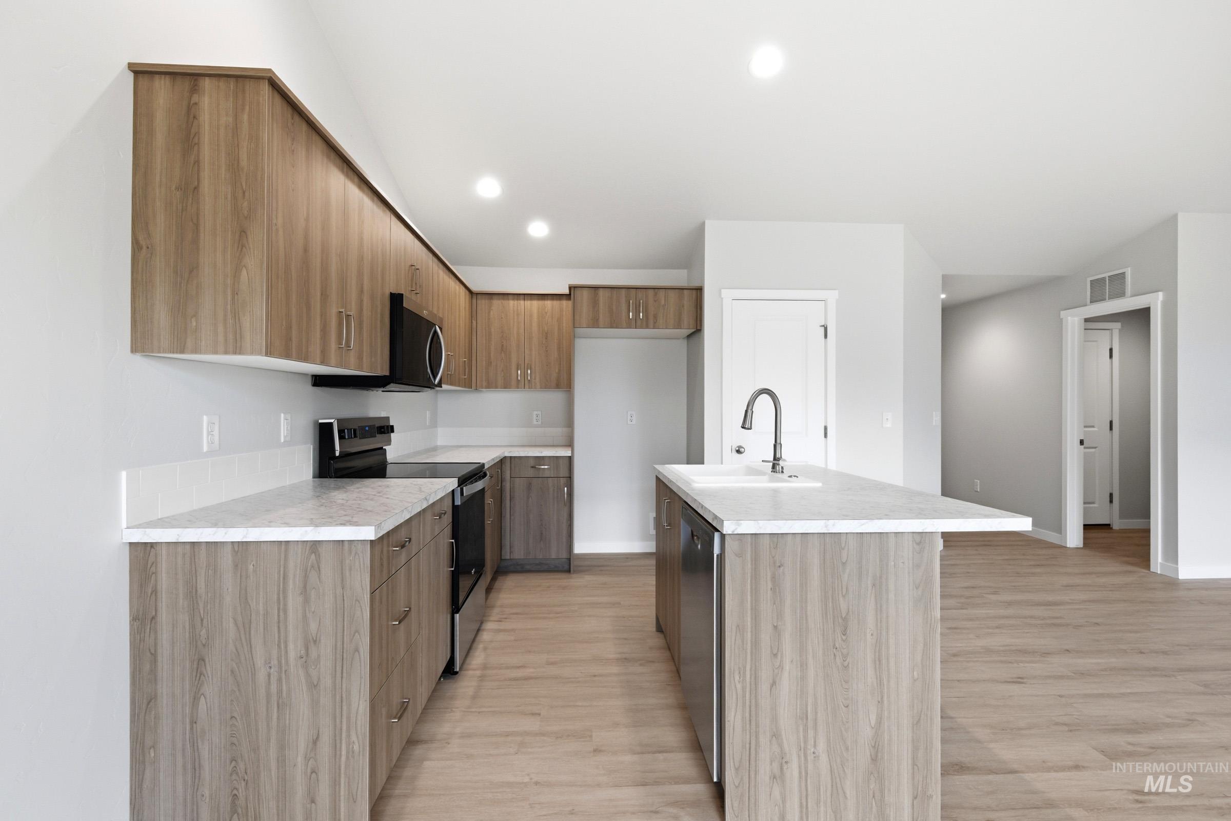 16632 North Shorthorn Loop Nampa, ID 83651 - Photo 6 of 17 Kitchen featuring wood-finish cabinetry, light-toned countertops, and a central island with an integrated sink
